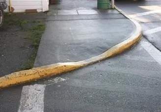 Narrow curb cut. The raised sidewalk edge (painted yellow) slopes down to the middle of a crosswalk.