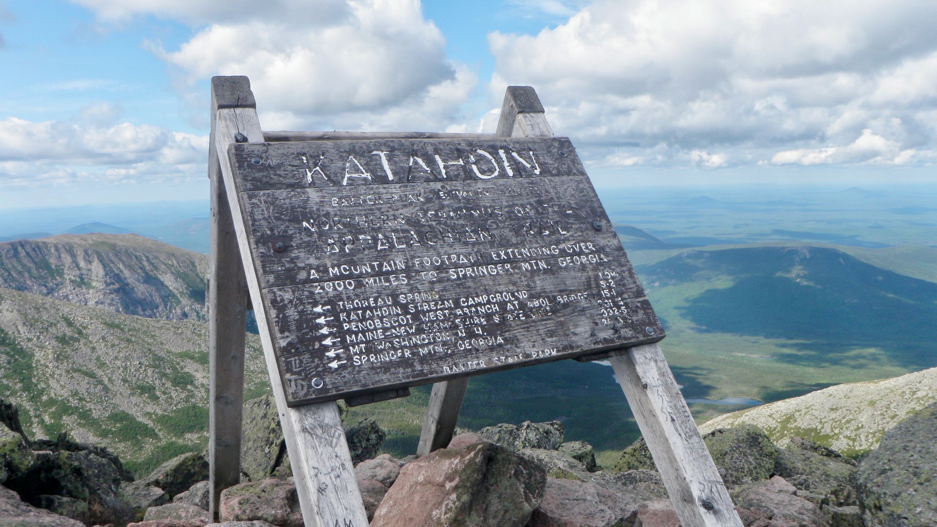 Freestanding, very weathered wood trail sign with faded white lettering