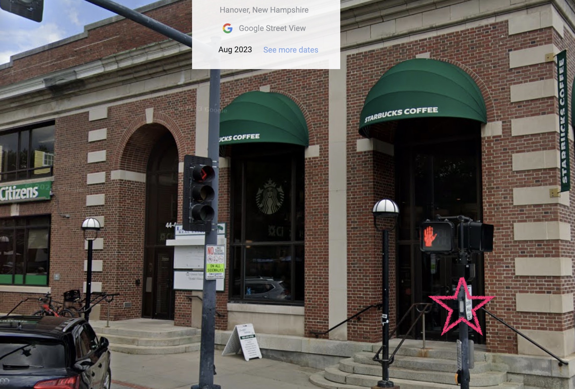 A Starbucks with a crossing light with a white blaze on its pole