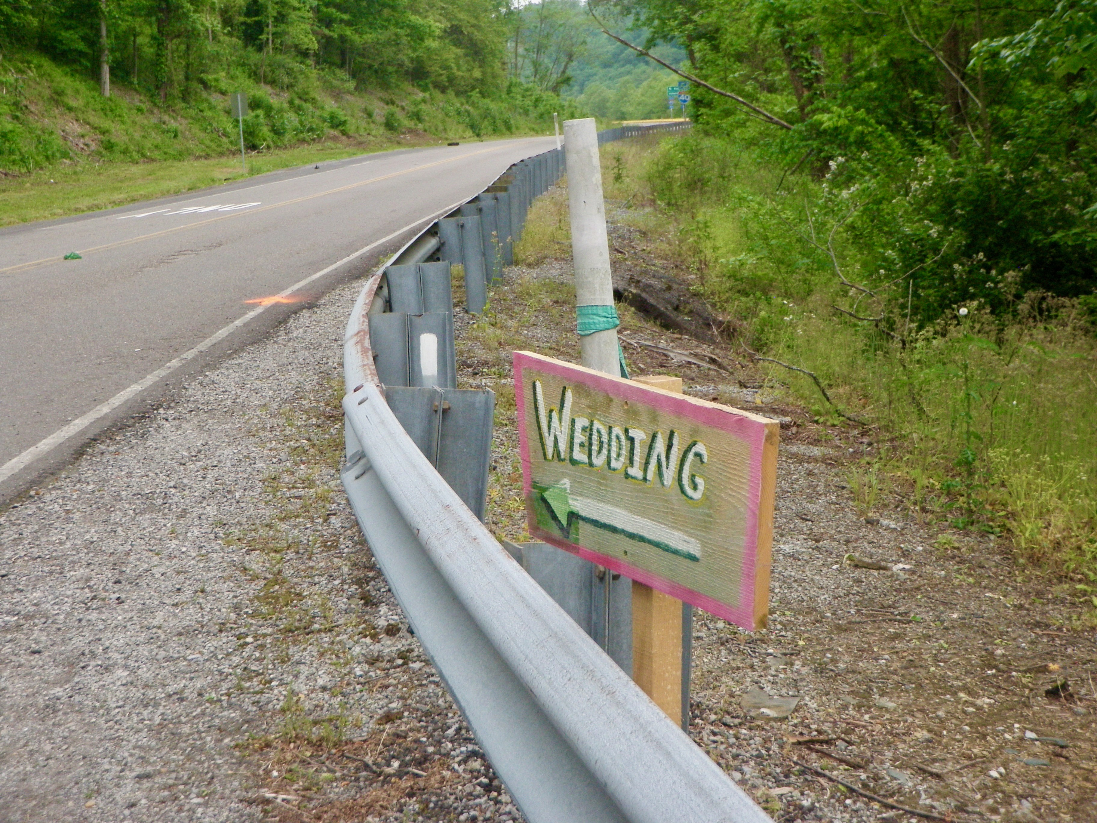 A rural highway with a white blaze on the guard rail next to a with an arrow to a wedding