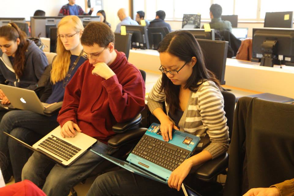 Four students sitting next to each other staring at their laptop own laptop.