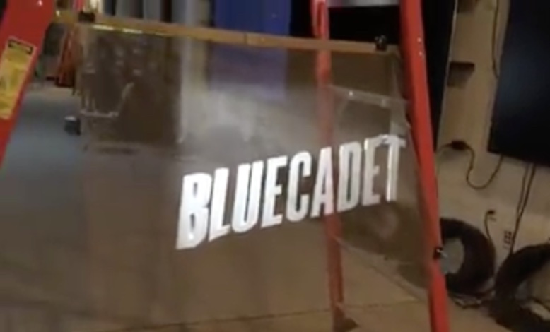 BLUECADET in all caps displayed on a nearly invisible screen, which is hung on a step ladder's spreader bar