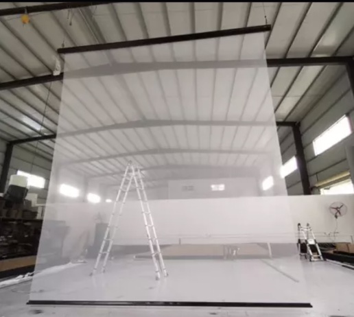 A semi-transparent floor-to-ceiling mesh screen hangs in the middle of a warehouse. The ladder behind the screen is clearly visible.
