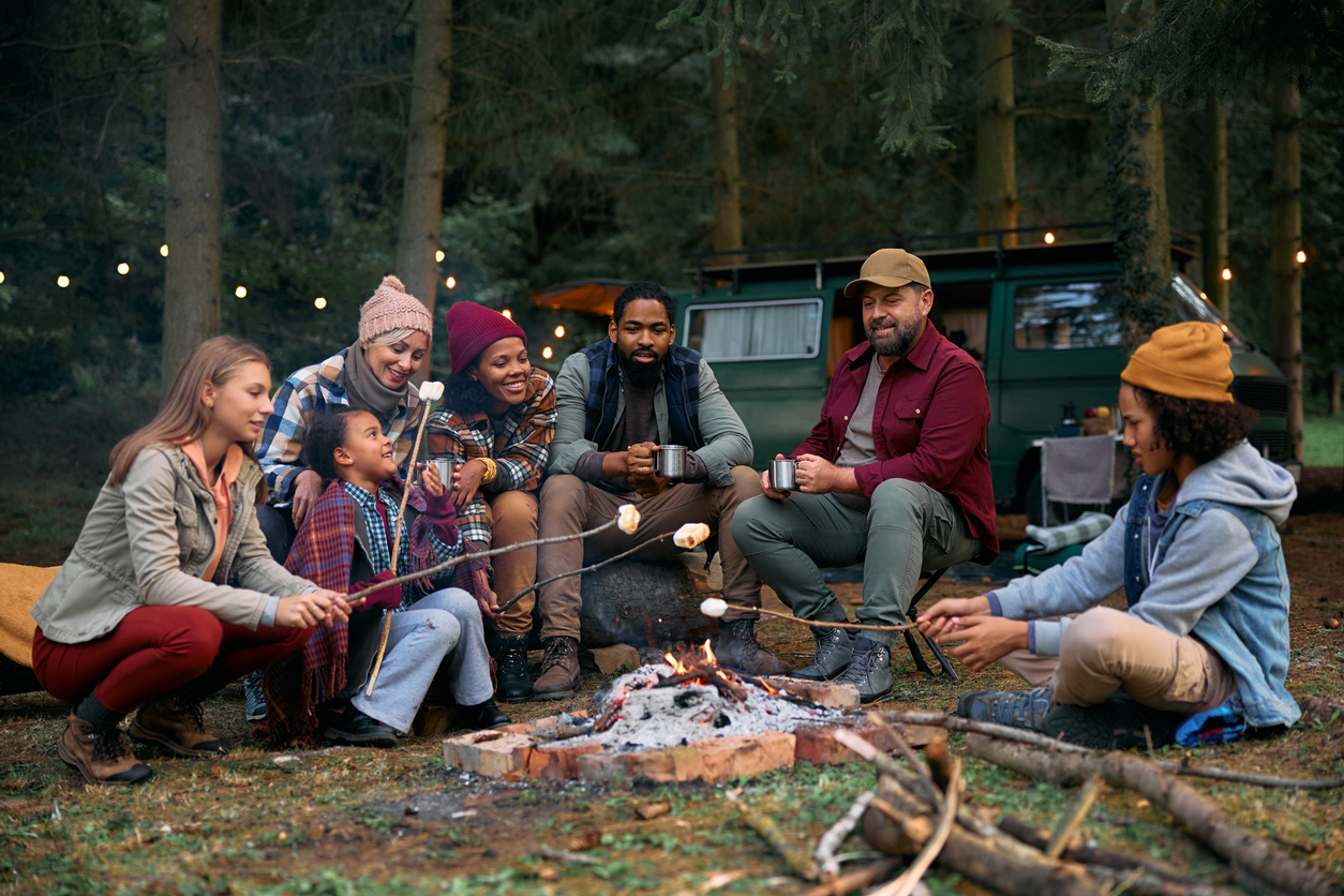 Multiracial families roasting marshmallows while gathering around campfire in the woods