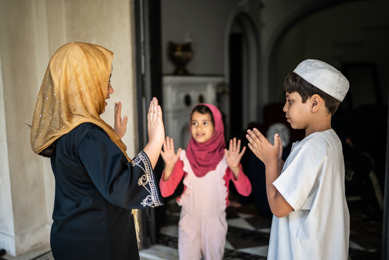 Two girls and one boy, all with traditional Muslim head coverings, playing a hand game at home in Lebanon
